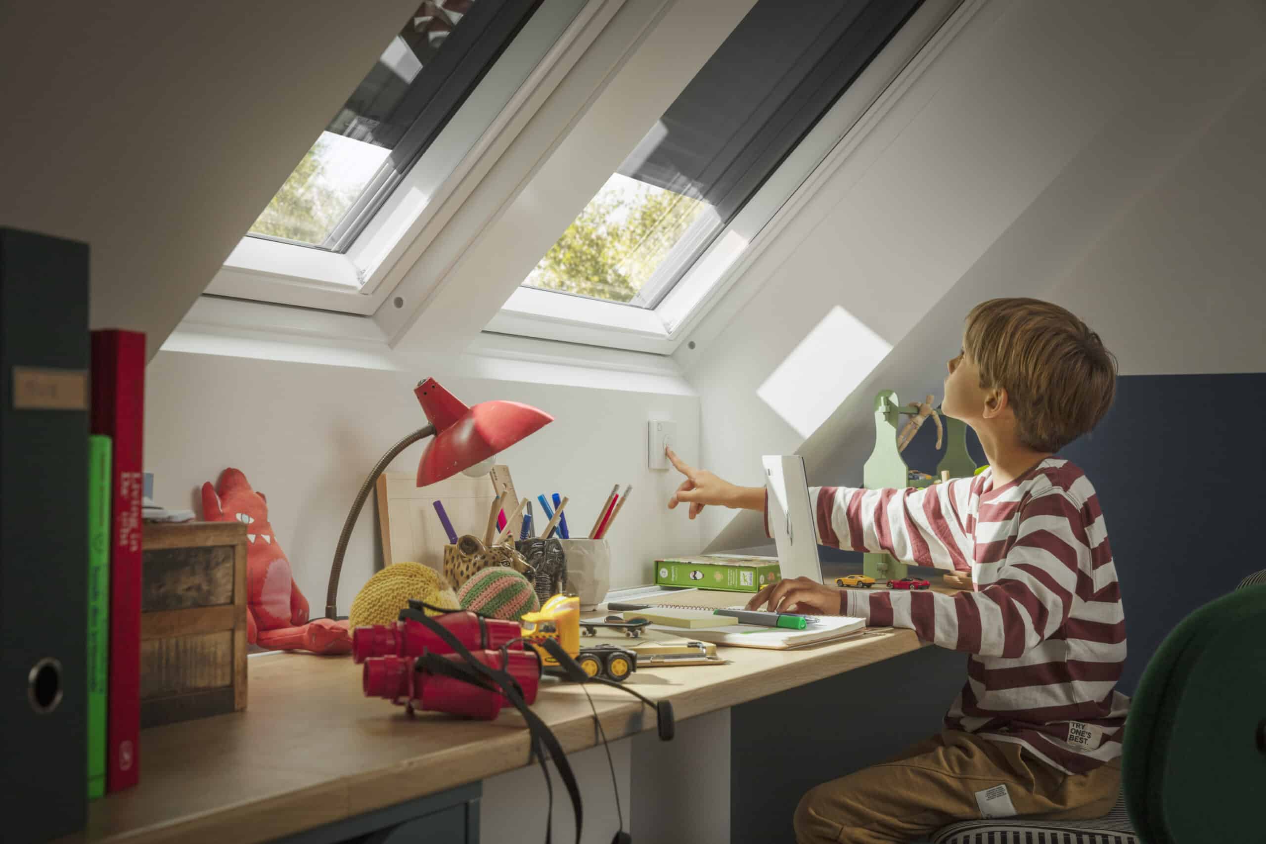 Espace de travail sous les combles avec plafond en pente et fen&ecirc;tres de toit VELUX ; enfant &agrave; son bureau.