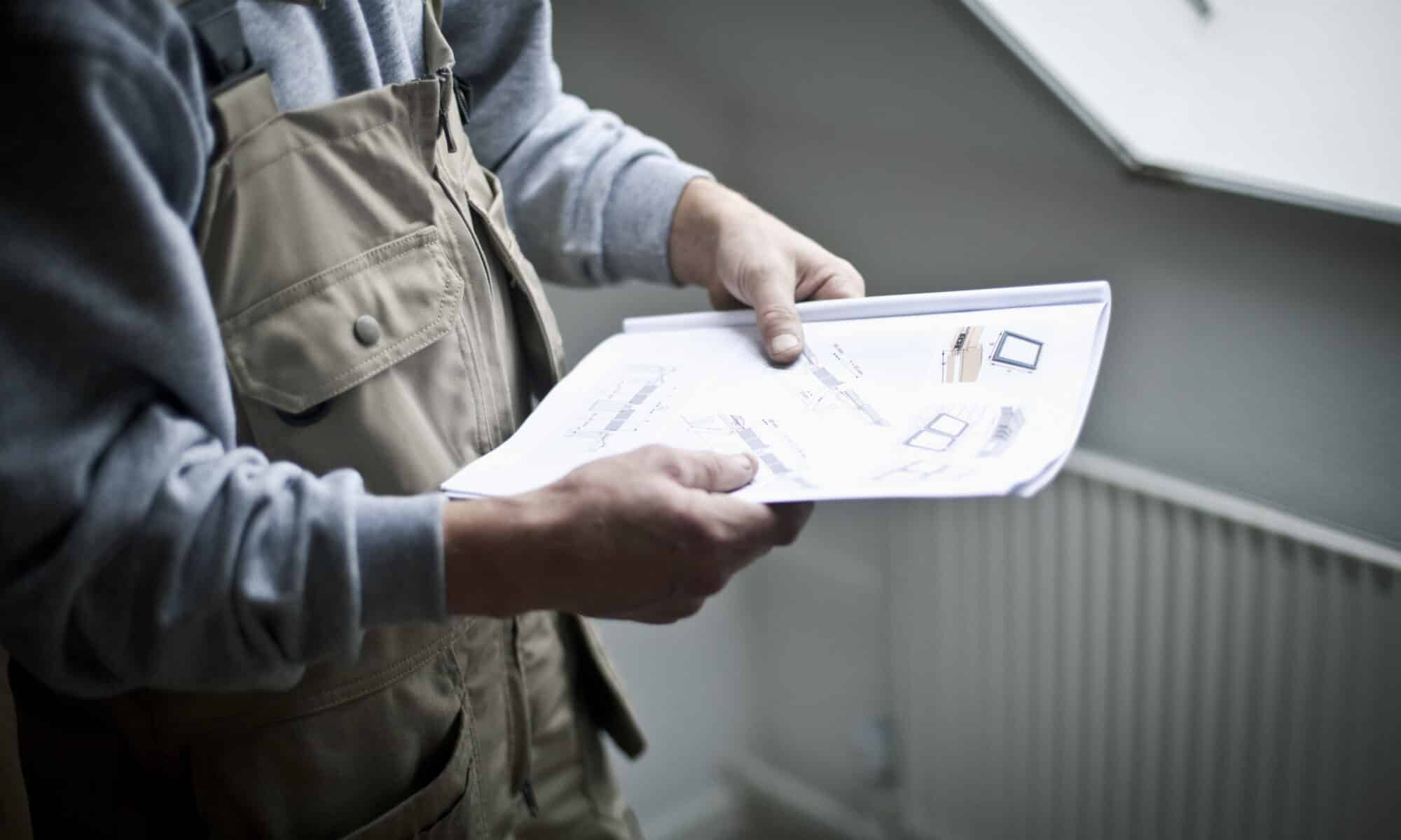 Un ouvrier du bâtiment examine des plans architecturaux près d'une fenêtre de toit VELUX fermée.