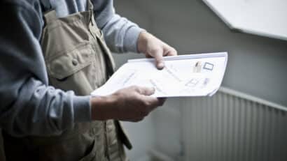 Un ouvrier du bâtiment examine des plans architecturaux près d'une fenêtre de toit VELUX fermée.