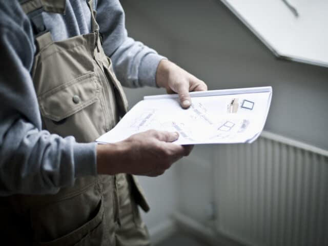 Un ouvrier du bâtiment examine des plans architecturaux près d'une fenêtre de toit VELUX fermée.