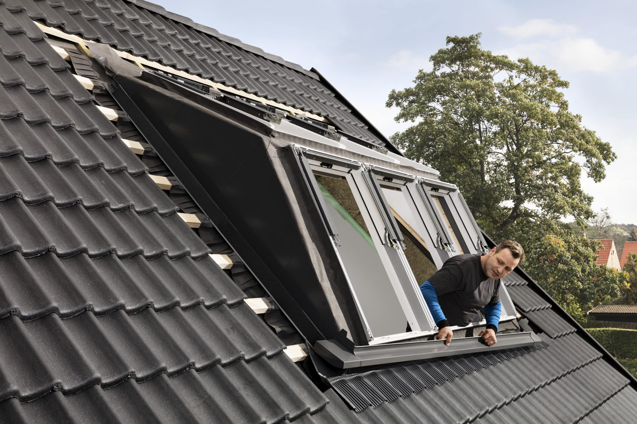 Installation de fen&ecirc;tres sur toit en tuiles fortement inclin&eacute;es avec des tuiles en c&eacute;ramique noires.