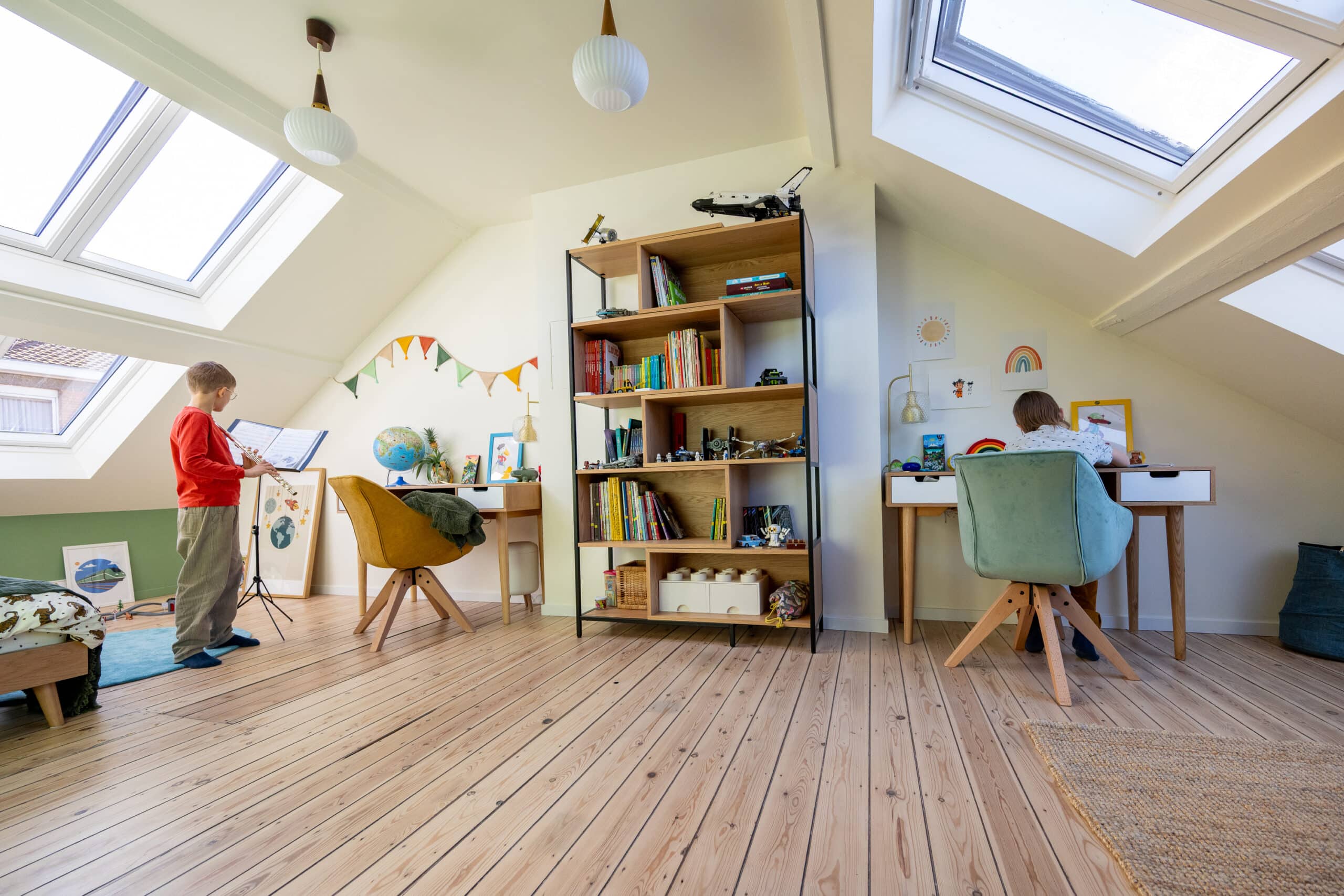 Chambre d'enfant sous les combles avec plafond en pente, grandes fen&ecirc;tres de toit, bureaux et biblioth&egrave;que.