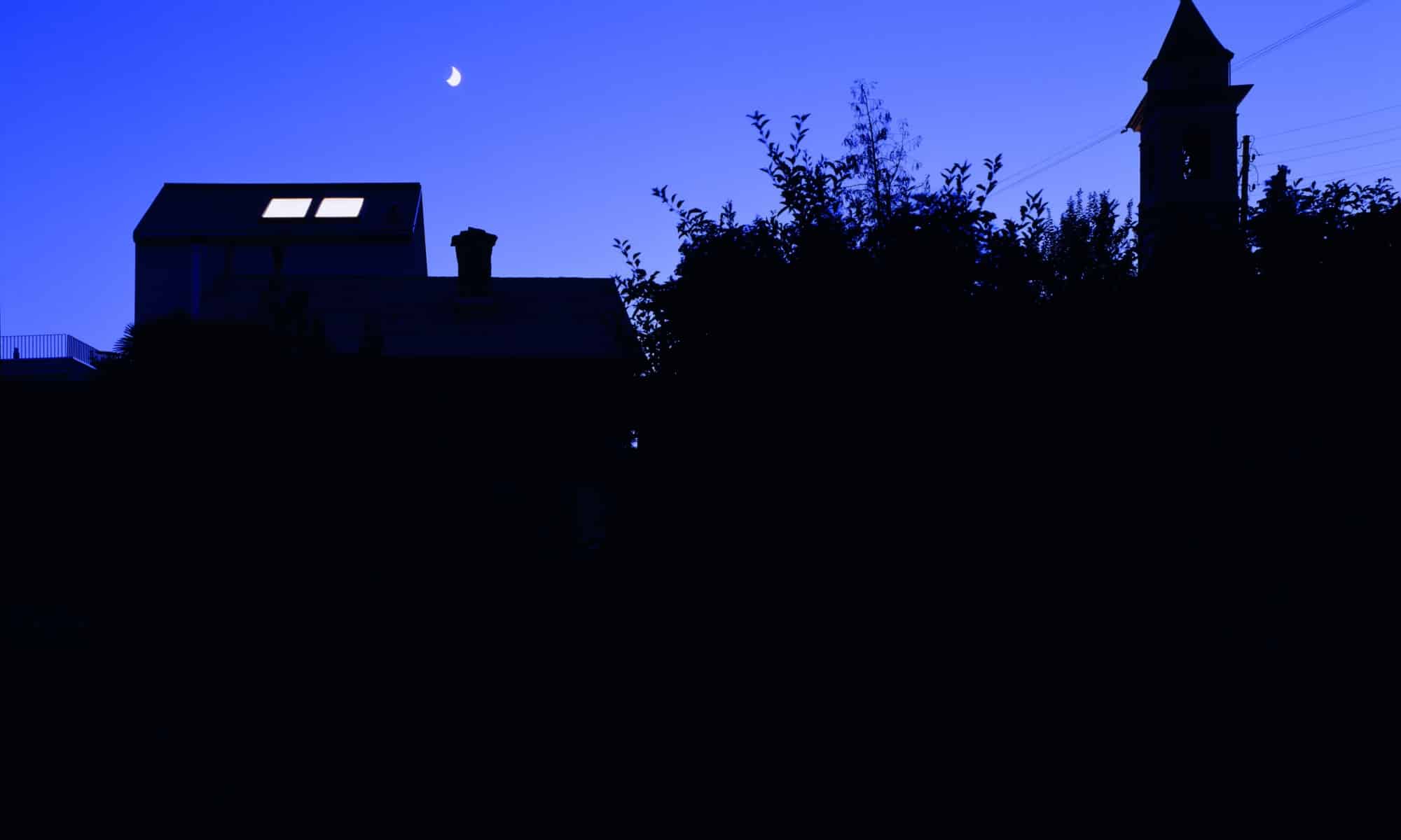 Bâtiment avec des fenêtres de toit illuminées sous un croissant de lune la nuit pour Hallowwen