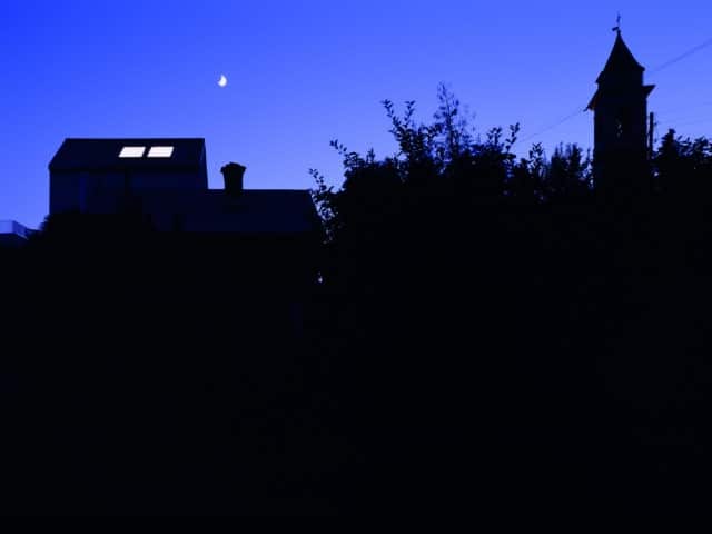 Bâtiment avec des fenêtres de toit illuminées sous un croissant de lune la nuit pour Hallowwen